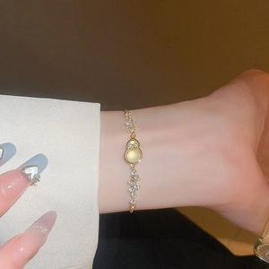 Macro shot of gold bracelet featuring a bow knot and cat-eye stone gourd charm