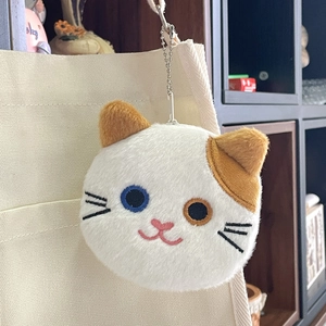 Detail of plush cat coin purse with odd-eyed design hanging on a canvas bag