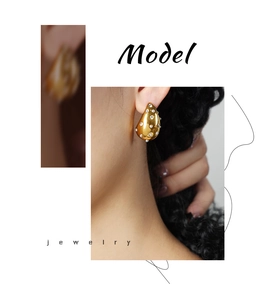 Close-up of golden teardrop earrings with white pearls worn by a fashion model