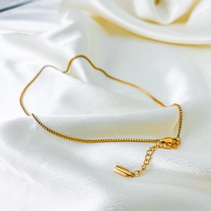 Detailed shot of golden box chain with lobster clasp on elegant white silk background
