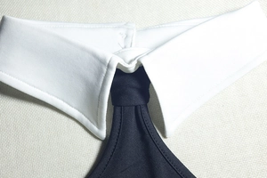 Detail of white shirt collar with fixed black tie accessory and neat stitching
