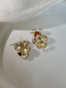 Détail de boucles d'oreilles grappes dorées avec perles en résine et nacre sur plat blanc