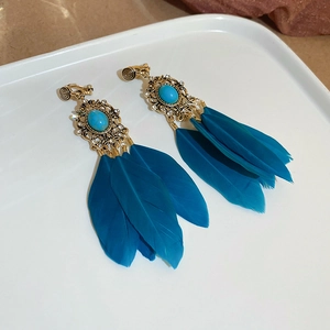 Détail de boucles d'oreilles dorées vintage avec turquoise bleue et plumes longues