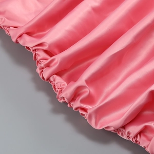 Détail du tissu en satin rose montrant la texture brillante et les coutures élastiques