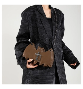 Close-up of brown bat-shaped gothic shoulder bag with chain and cross on black blazer