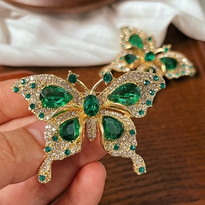 Close-up of golden butterfly brooch with green gems and clear crystals on wings