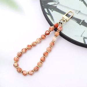 Detail of beaded phone strap featuring orange marble beads and gold metal accents