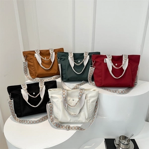 Five nylon tote bags in various colors with stylish wide woven shoulder straps on white stands