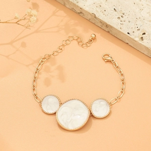 Flat lay of gold chain bracelet featuring three round white marble pendants on stone