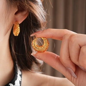 Macro detail of 18k gold plated round hollow textured hoop earrings worn by a model