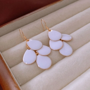 Macro view of white enamel teardrop earrings with gold trim in a beige velvet jewelry box