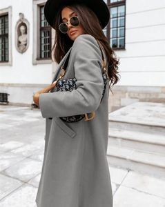 Side view of long grey wool coat worn by a model against classic white architecture