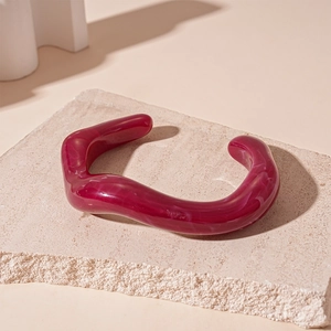 Detailed shot of dark red marble resin cuff bracelet on minimalist beige stone tray