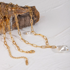 Detailed shot of baroque pearls on gold stainless steel chain draped over a brown rock