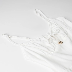 Détail du caraco blanc avec design plissé sur le buste et embouts dorés délicats
