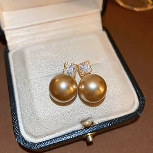 Détail de boucles d'oreilles carrées en zircon avec grandes perles dorées dans un écrin