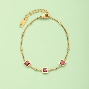 Detail of gold titanium steel bracelet with three red square gemstones on green background