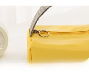 Detail der gelben Kosmetiktasche mit grauem strukturiertem Griff und rundem Metallreißverschluss
