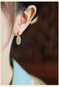 Close-up of gold Chinese style earrings featuring oval green jade and enamel flower charms