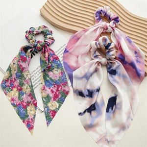 Flat lay of colorful tie-dye and floral fabric scrunchies with long ribbons on beige background