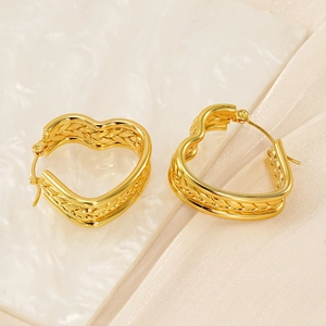 Detailed macro view of gold heart earrings with woven texture on white tile and beige fabric