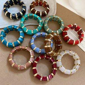 Flat lay of colorful acrylic resin bracelets with gold spacers on a minimalist background