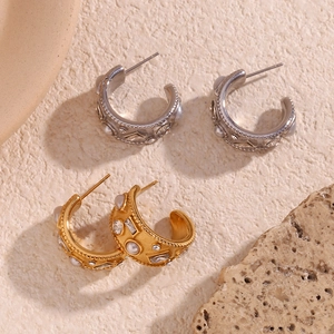 Detail of C-shaped 18K gold and silver pearl earrings on a natural stone background