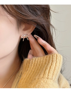Close-up of elegant bow-shaped stud earring worn by model with metallic finish