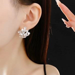 Close-up of a model wearing minimalist silver flower earrings on a black background