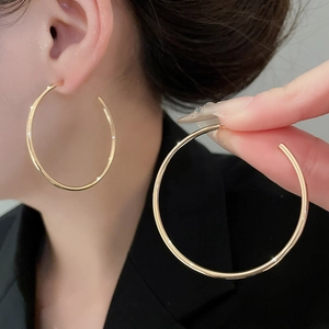 Close-up of a large gold hoop earring worn by a model against a dark suit background