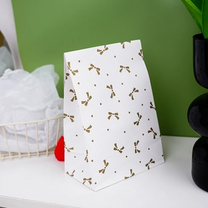 Close-up of a white paper gift bag featuring elegant gold bow patterns and gold polka dots