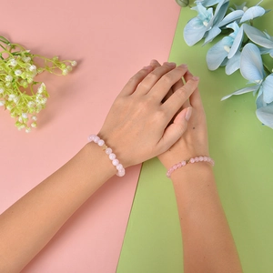 Pink beaded bracelet with a golden heart pendant worn by a model against floral background