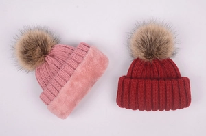 Detailed view of pink and dark red knit beanies with fluffy faux fur pom-poms