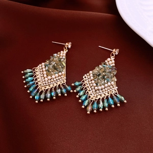 Detailed macro view of vintage gold earrings with emerald crystals and blue teardrop tassels