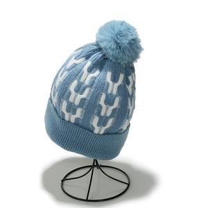 Detail of blue knitted beanie with white jacquard pattern and large faux fur pom-pom