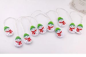 Detail of LED snowman fairy light with white body, green hat, and festive red scarf