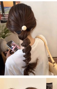 Close-up of brown spiral hair tie with a white decorative bead on a braided ponytail