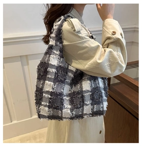 Detail of black and white plaid tote bag featuring tweed texture and fringe trim