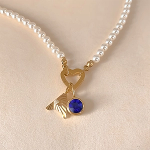 Détail d'un collier de perles avec un fermoir en cœur doré et un pendentif en cristal bleu