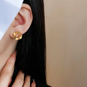 Golden twisted hoop earrings with matte finish shown on model in a minimalist style