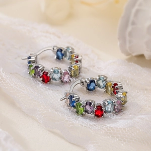Macro shot of silver hoop earrings featuring colorful zircons on white lace fabric