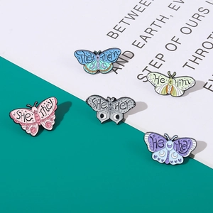 Dettaglio di spille a farfalla colorate in smalto con varie incisioni di pronomi