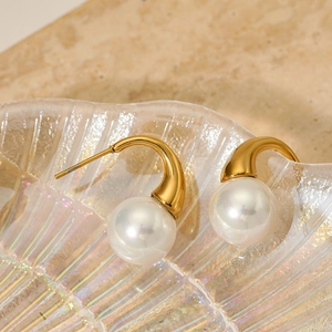 Elegant gold-plated stainless steel earrings with large round pearls on a glass tray