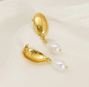 Macro detail of French vintage 18K gold earrings with hanging teardrop pearls on ceramic tray