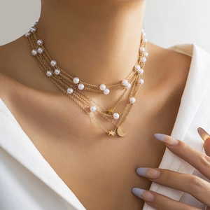 Detail of layered gold chain necklace with faux pearls and star moon pendants on model