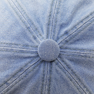 Detailed close-up of light blue denim baseball cap crown showing stitch lines and top button