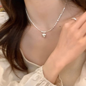 Collar vintage de plata con corazón, perlas brillantes y cadena texturizada en una modelo