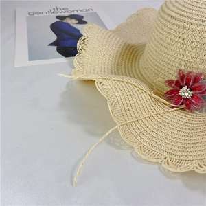 Detail of beige straw hat with wavy lace edges, red flower ornament, and crystal studs