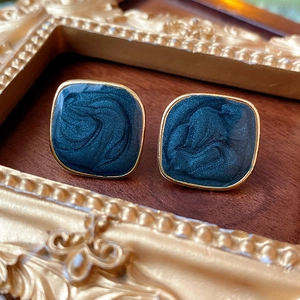 Detail of square dark green enamel earrings with gold border on a vintage frame