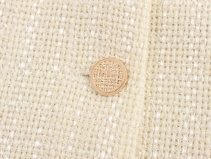 Vista macro del tessuto in tweed crema e di un bottone dorato con trama a rilievo sul blazer